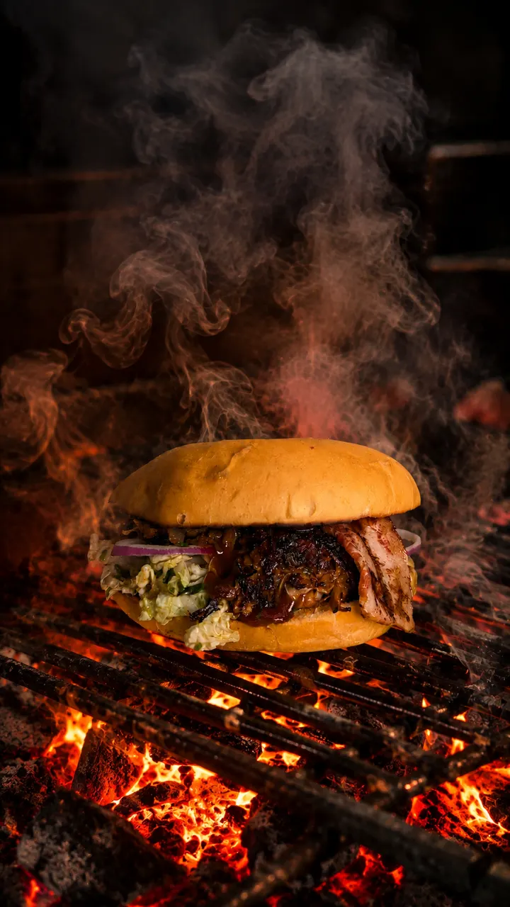 Burger de porc effiloché posé près des braises d’un grill, dans la fumée